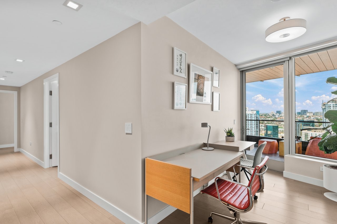 Furnished home office with a red leather chair and downtown skyline views through floor-to-ceiling windows.