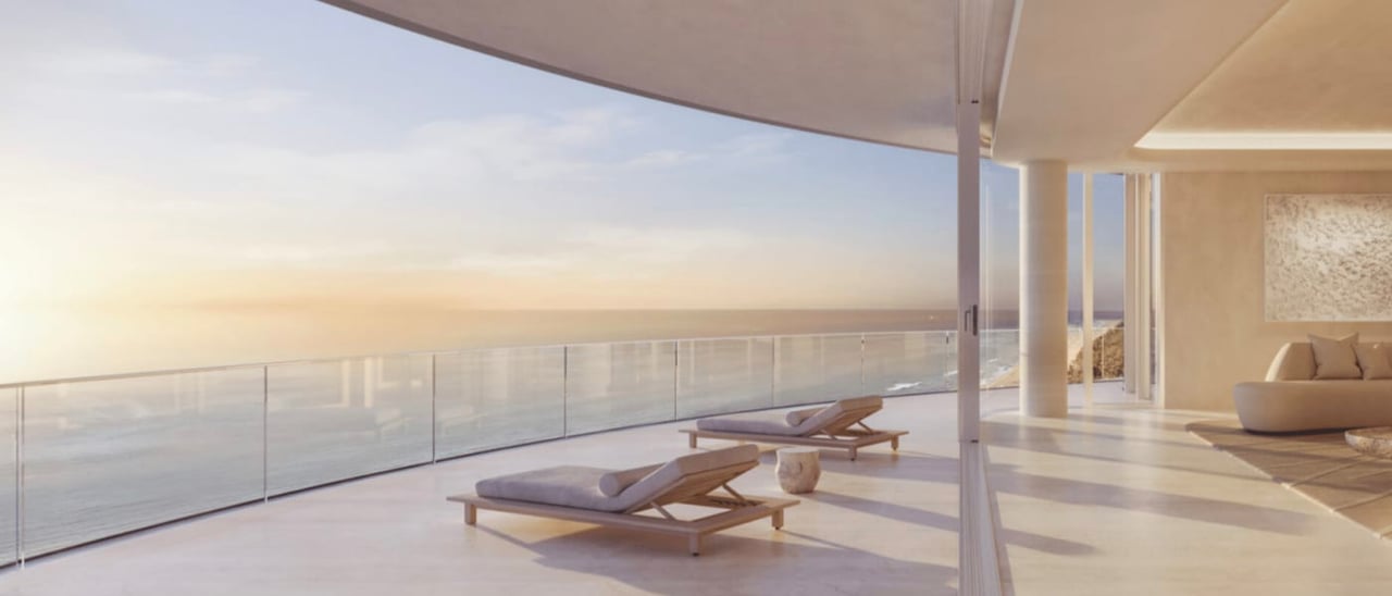 Oceanfront condominium terrace with glass railing, lounge chairs, and sunset views.