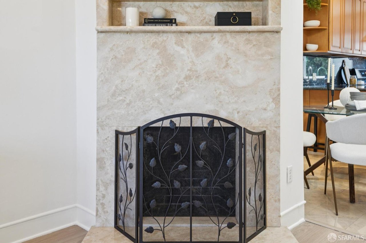 Marble fireplace with an ornate black metal screen beside a furnished dining area.