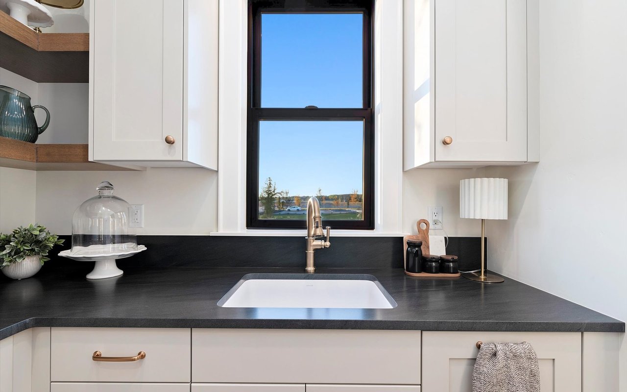 Butlers pantry with white cabinets, black countertops, and a window over the sink