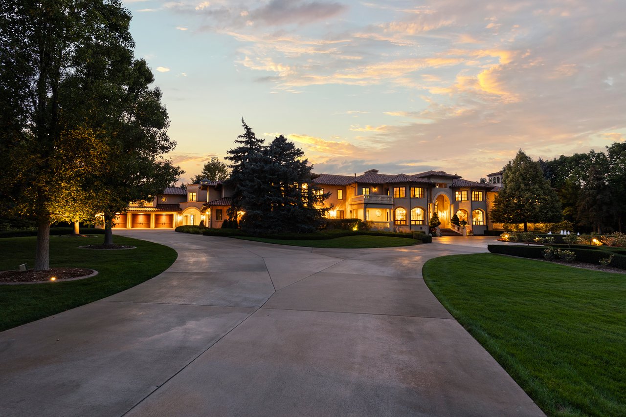 Mediterranean-style estate glowing at dusk, viewed across a sweeping driveway and manicured grounds.