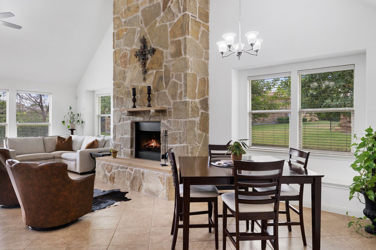 Living and dining area with a tall stone fireplace, sectional sofa, and dark wood table by large windows.