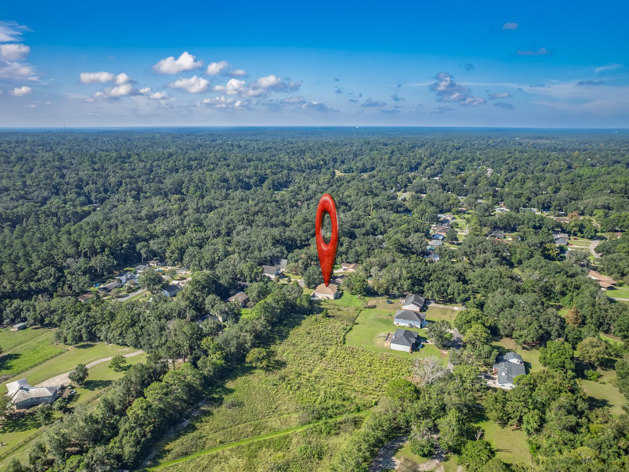 Aerial view of a home site marked by a red pin amid wooded surroundings.