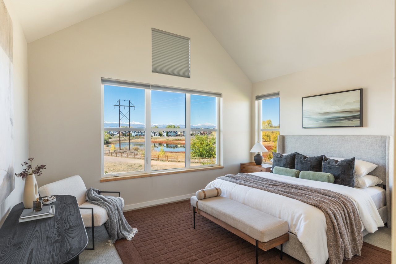 Primary bedroom with a vaulted ceiling, upholstered bed, and wide windows overlooking open space
