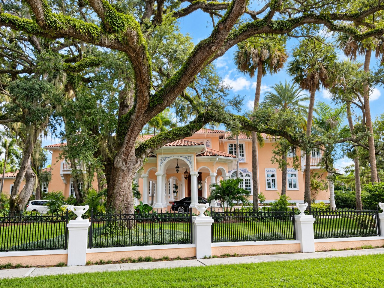 Peach two-story home with an arched entry, framed by mature trees and palms.