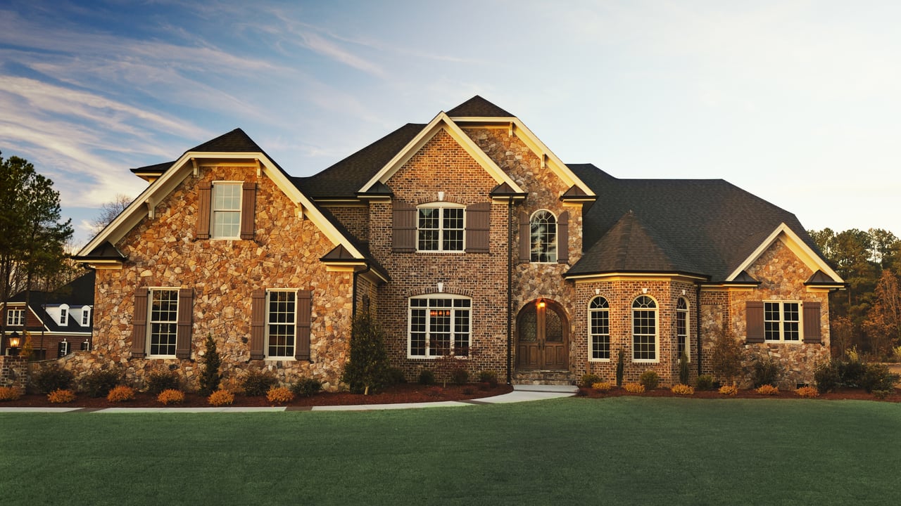 Two-story brick and stone home with an arched entry and broad front lawn.