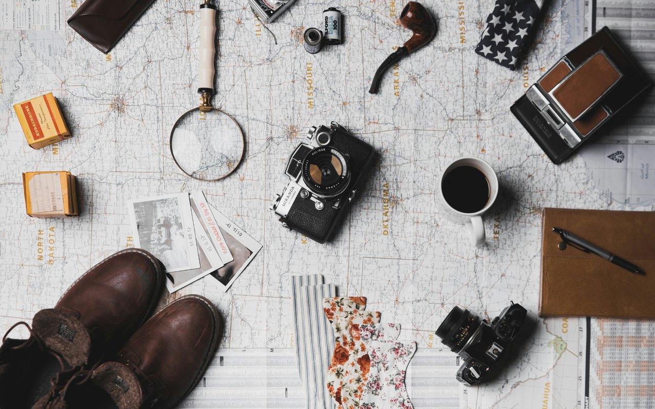 Travel accessories, vintage cameras, leather boots, and coffee arranged on a road map.