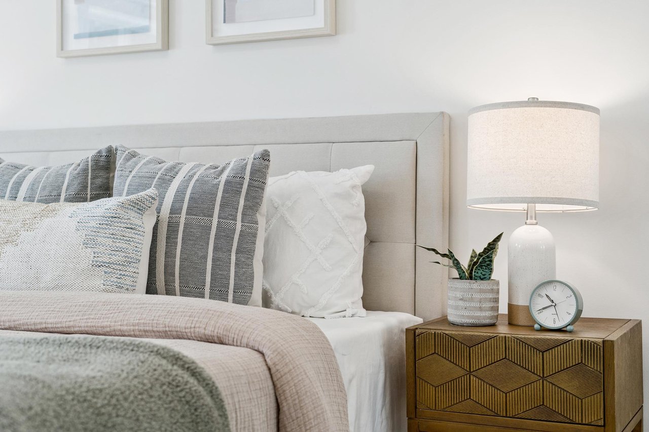 Staged bedroom with a light upholstered bed and geometric wooden nightstand.