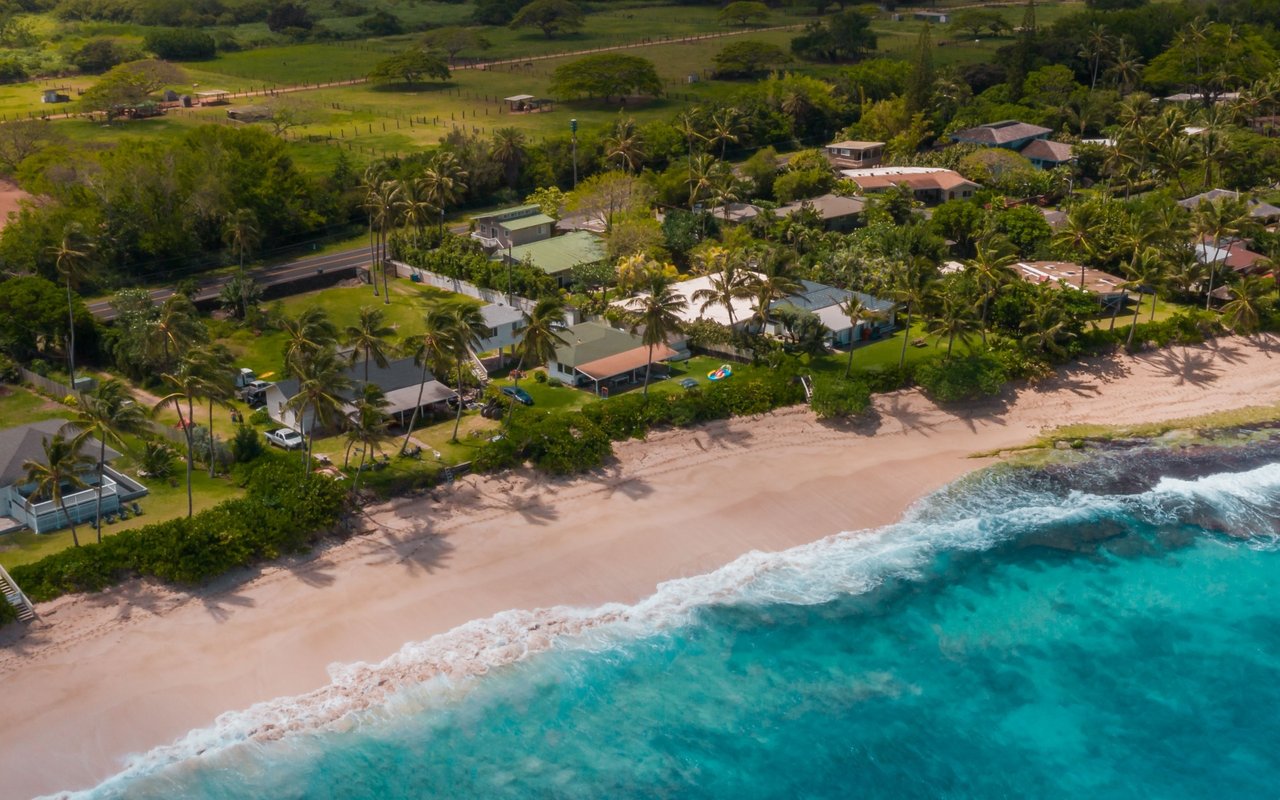 Aerial view of beachside homes and palms beside a sandy shore and turquoise ocean.