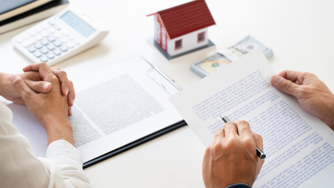 People sign real estate paperwork beside a house model and calculator.