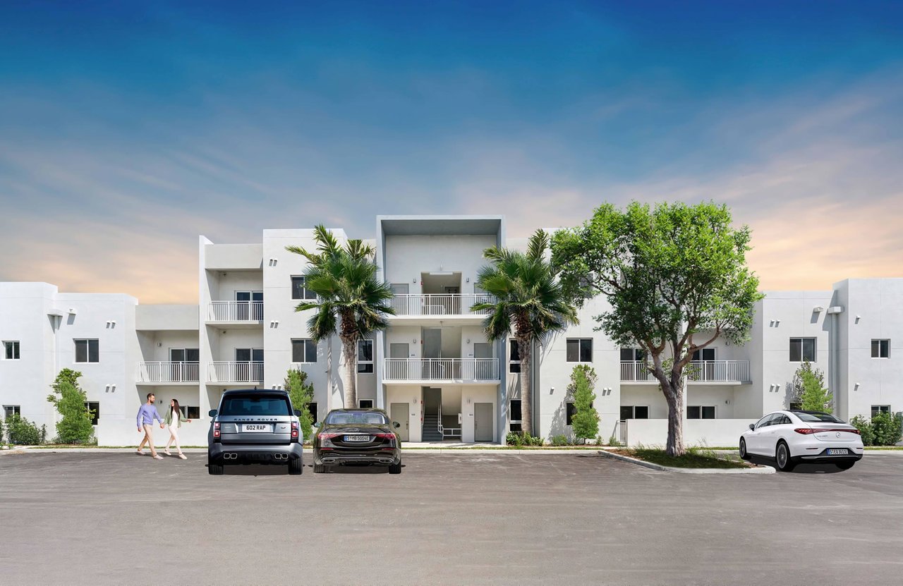 Modern white apartment building with balconies, palm trees, and parked cars at sunset.
