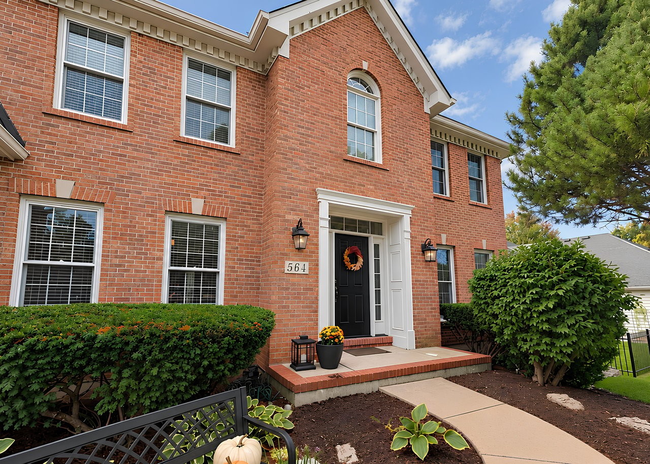 Two-story red-brick house with white-trimmed windows, black front door, and landscaped entrance decorated for autumn.