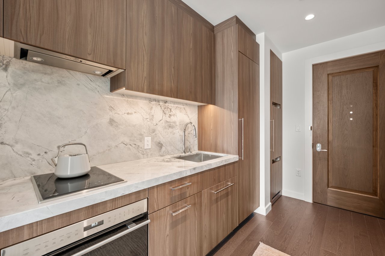 Modern kitchen with warm wood cabinets, veined stone counters, and a built-in cooktop and oven.