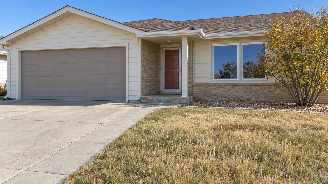Cream-sided ranch house with a buff-brick entry, attached garage, dry lawn and a small yellow-leaved serviceberry beside the front window.