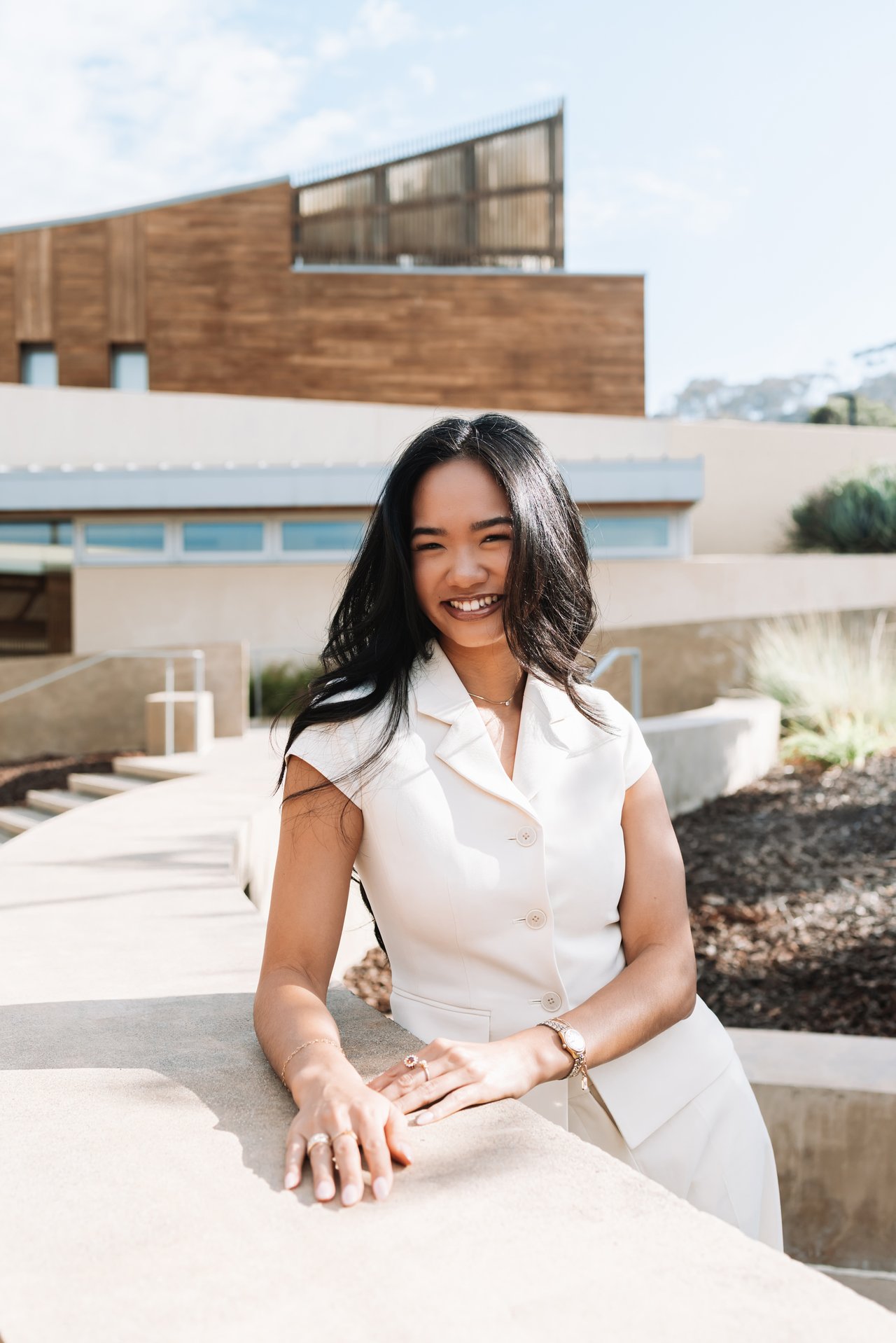 Smiling woman in a white sleeveless suit poses in front of a modern home.