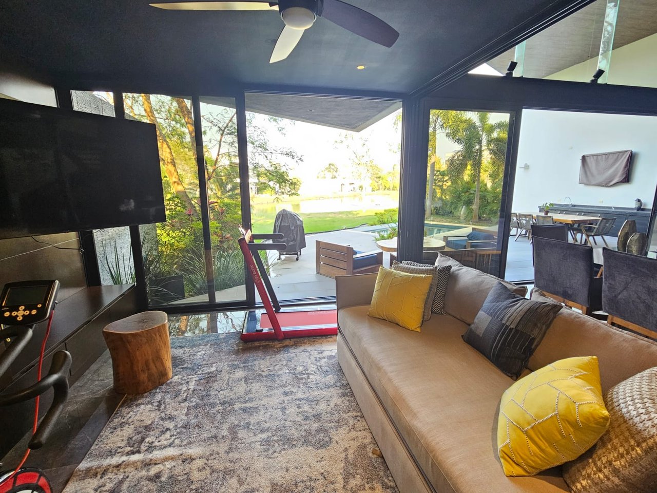 Living room with a beige sofa and yellow pillows overlooking a patio, pool, and garden.