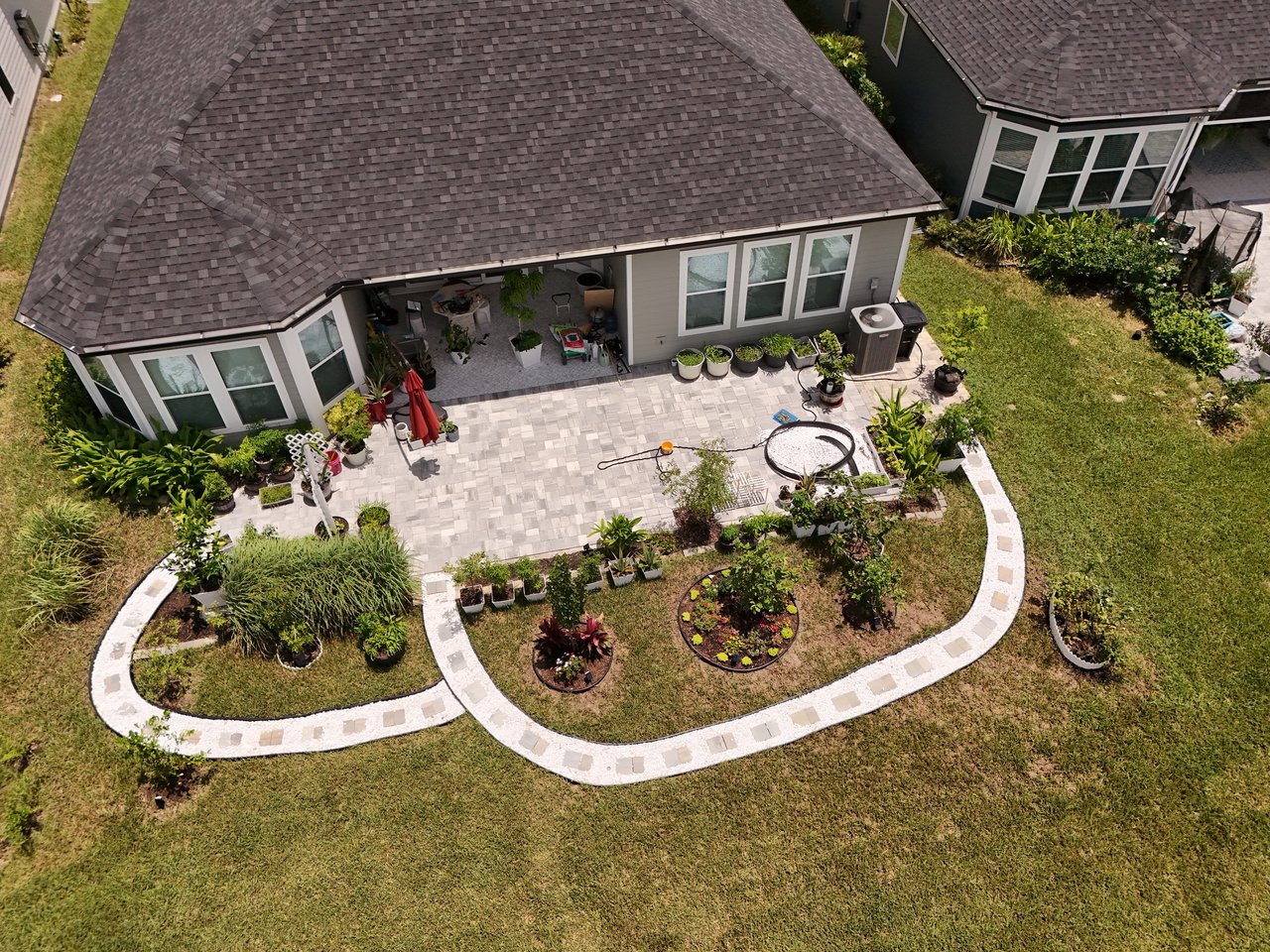 Aerial view of a home's backyard patio, with potted plants and curved stone paths through the lawn.