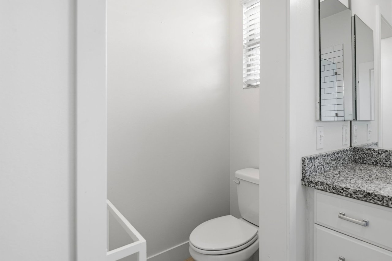 Bathroom with toilet, granite-top vanity with storage, and mirrored medicine cabinet