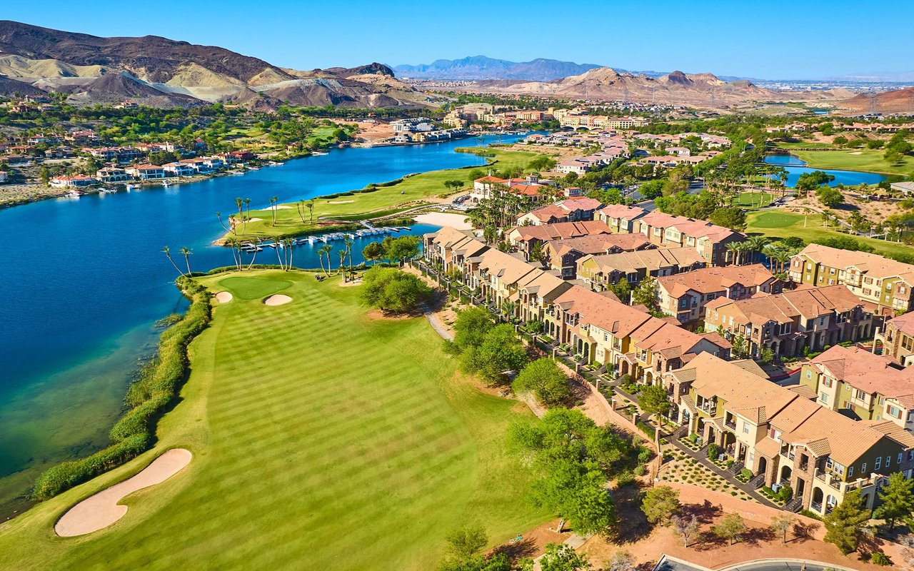 Waterfront homes beside a golf course and lake, with desert mountains in the distance.