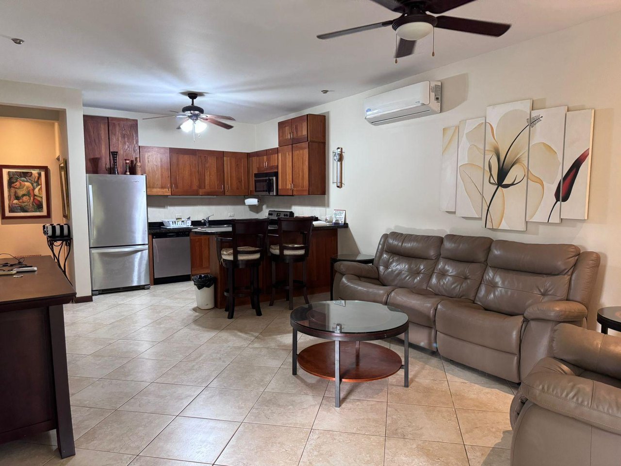 Open-plan condo living room with a leather sectional beside a wood-cabinet kitchen and breakfast bar.