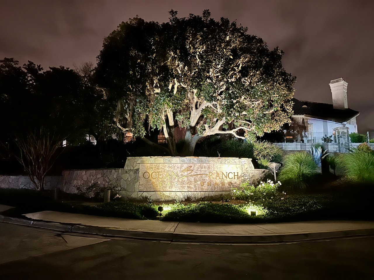 Ocean Ranch sub-community rear entry monument in Bear Brand, Laguna Niguel — illuminated stone signage framed by mature trees