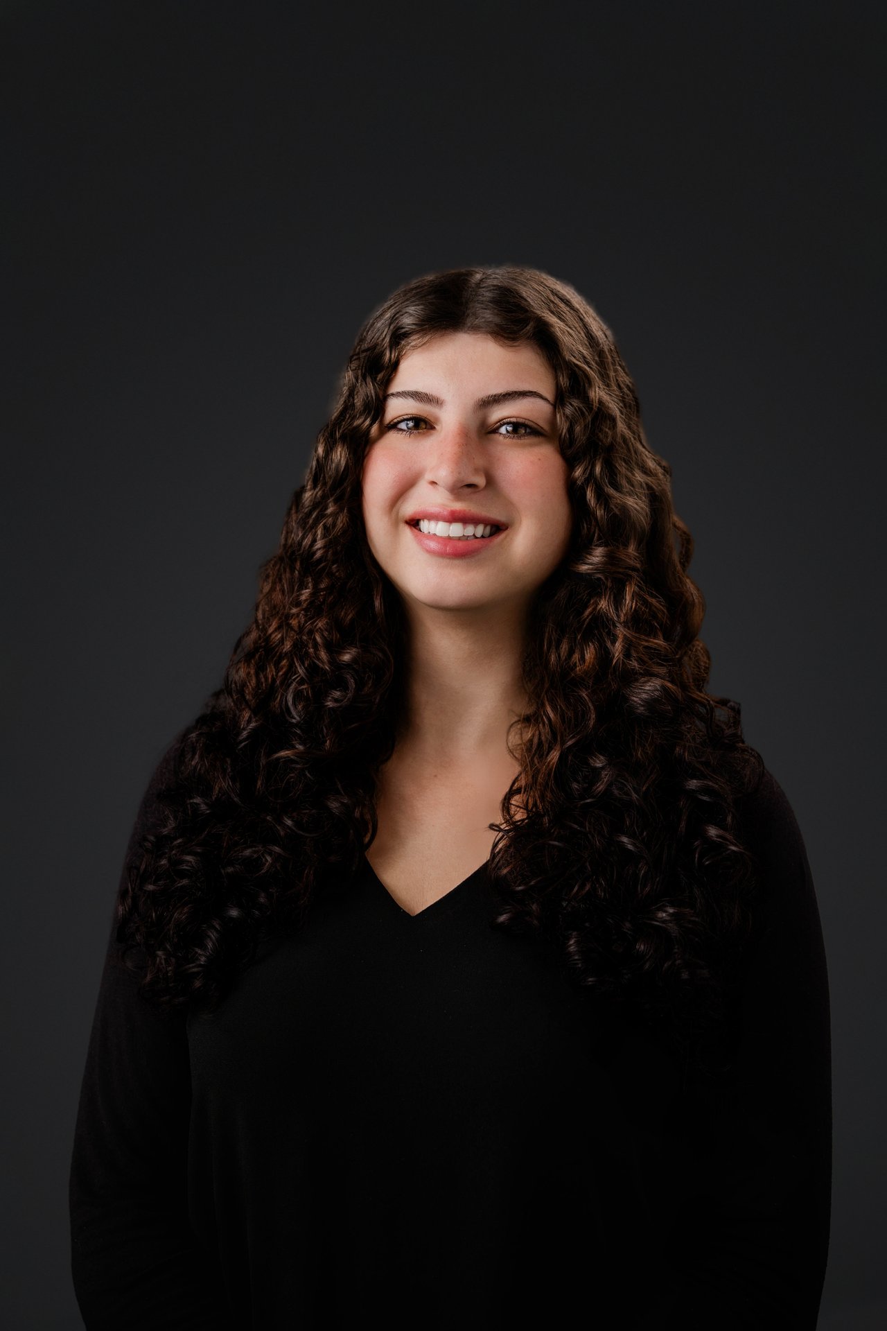 Maria Palazzolo smiling in a black top, with long curly brown hair.