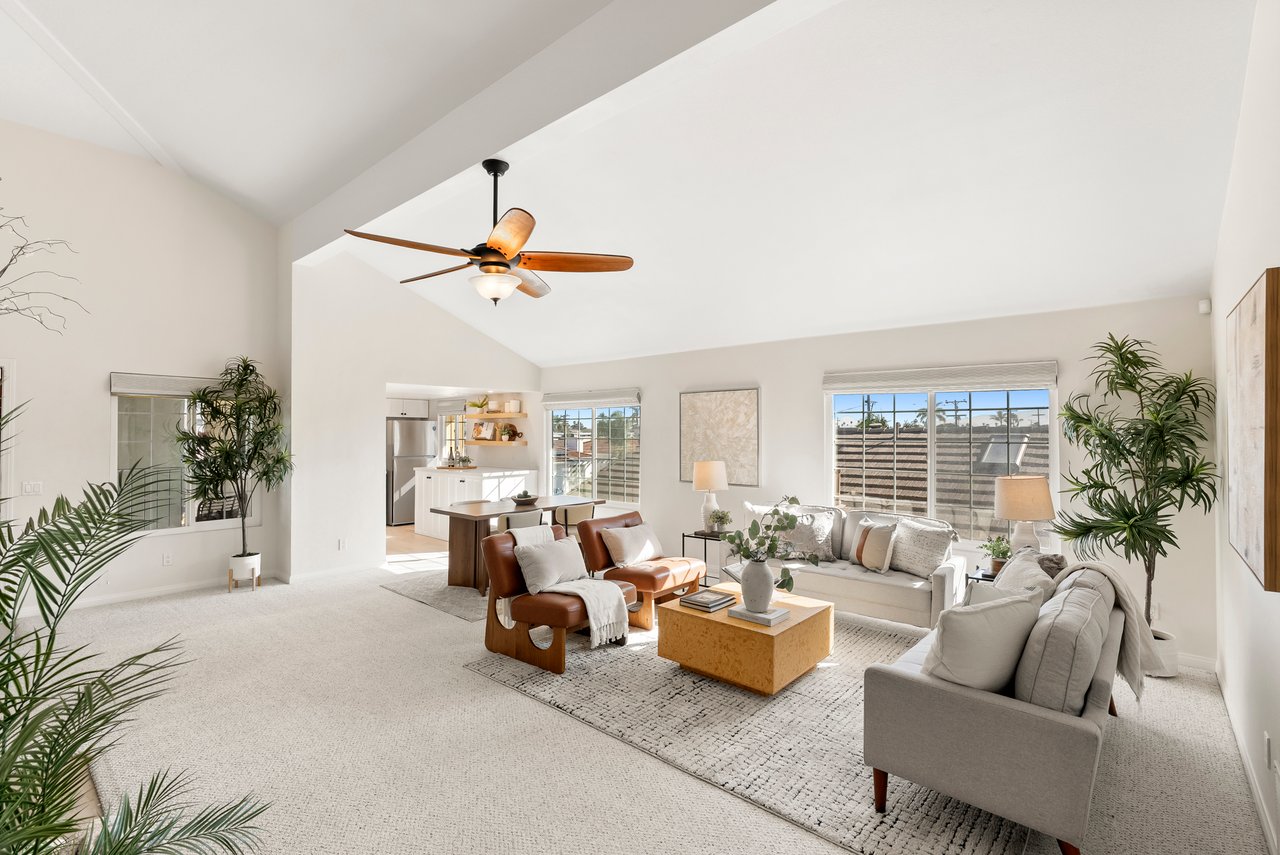 Vaulted living room with pale sofas, a wood coffee table, and an open kitchen.