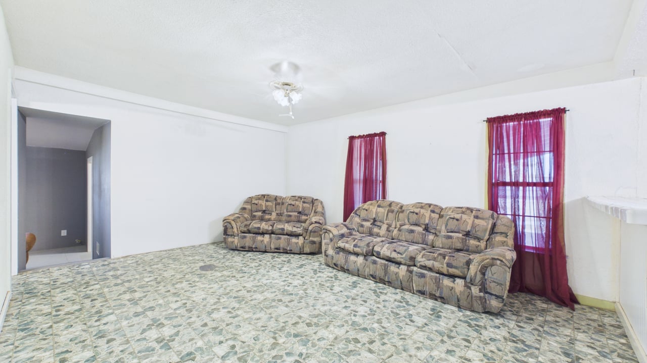 Living room with two patterned sofas, tiled flooring, and burgundy curtains.