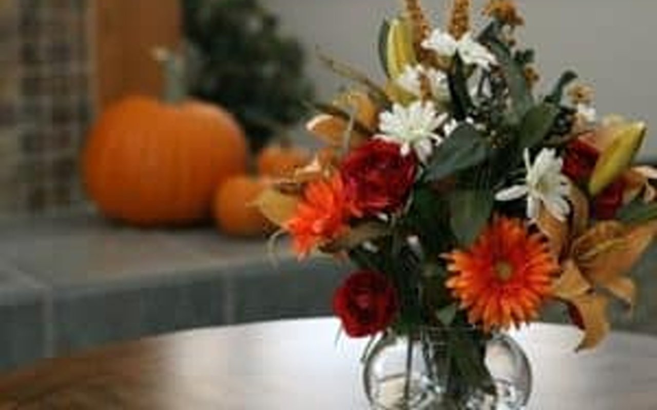 Fall flowers in a glass vase with pumpkins in the background.