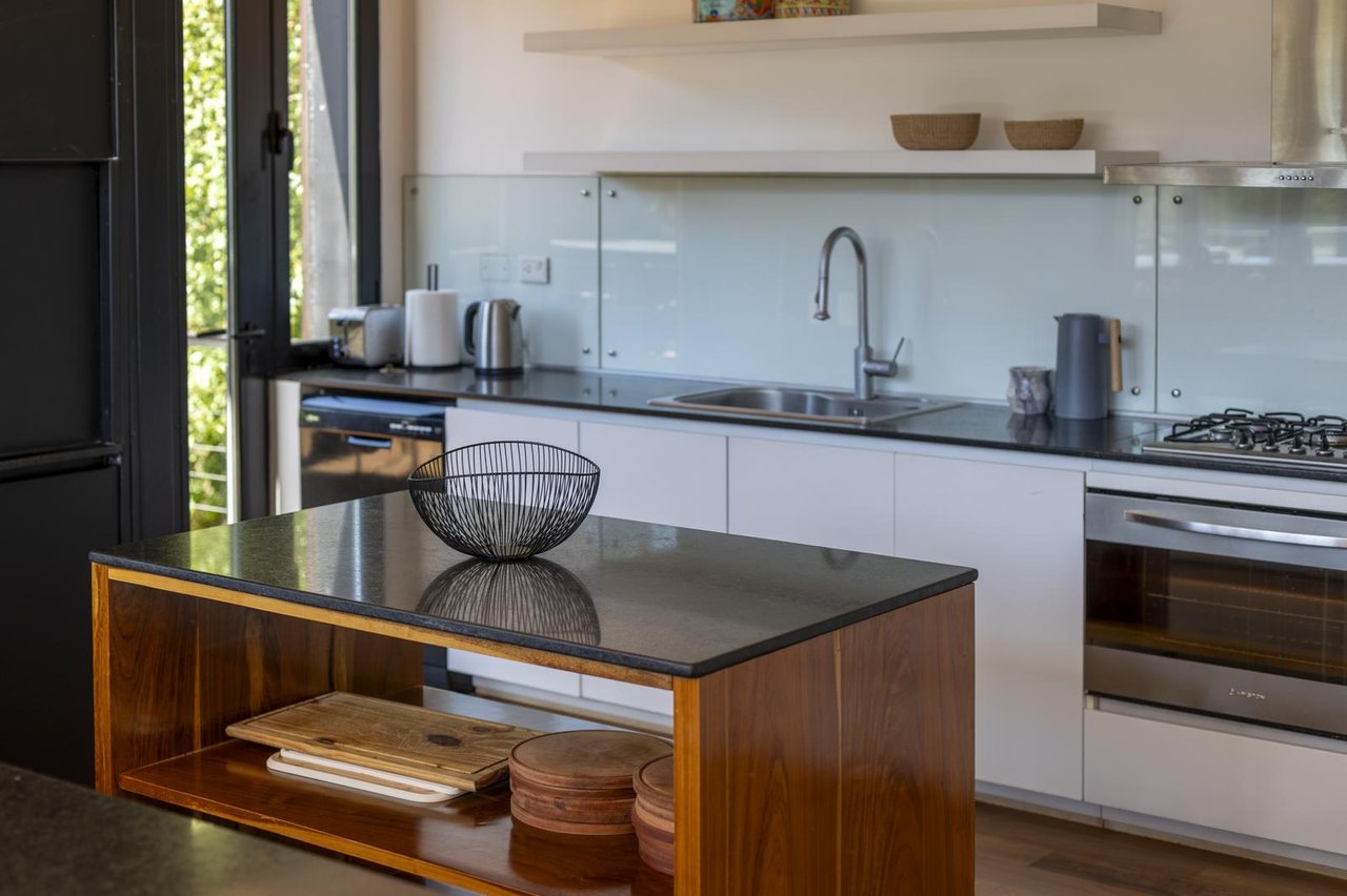 Modern kitchen with a wooden island, dark stone counters, and a pale glass backsplash.