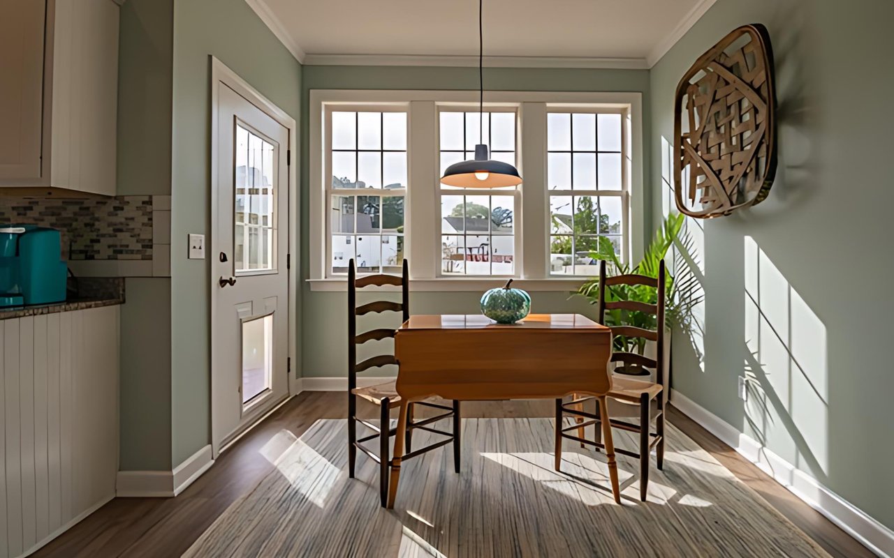Dining area with a wooden table, pendant light, and large sunlit windows.