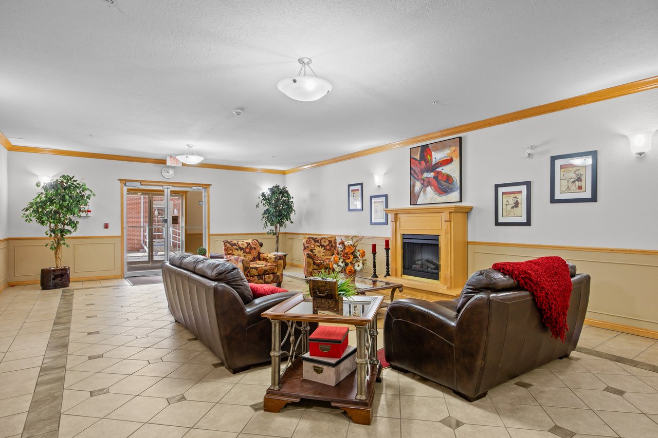 Communal lounge with leather sofas, patterned armchairs, and a fireplace beside glass entrance doors.
