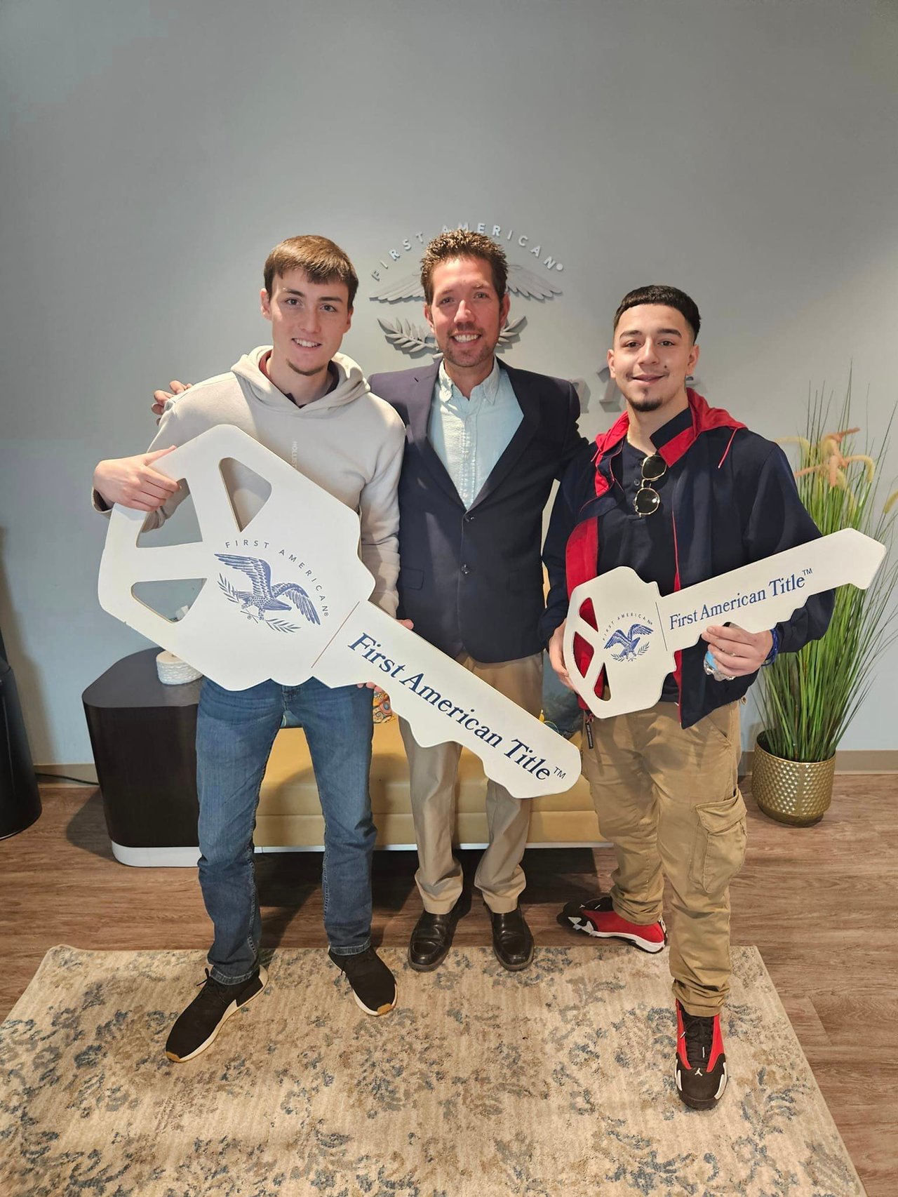 Three men pose with oversized First American Title keys in front of a First American sign.
