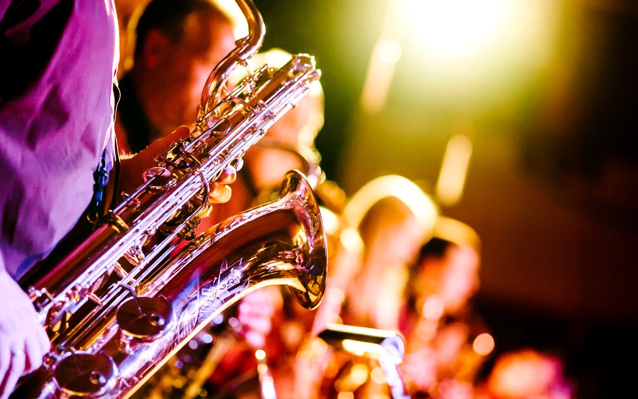 Saxophonists perform onstage under bright amber and purple lights.