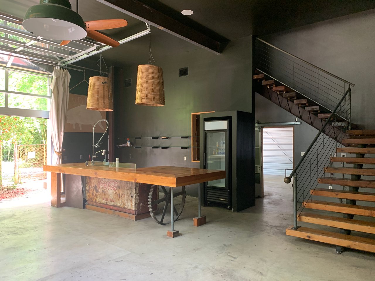Open main-level flex space at 640 Tillery Street in East Austin with a wood-top bar, open-tread stair, and a glass overhead door.