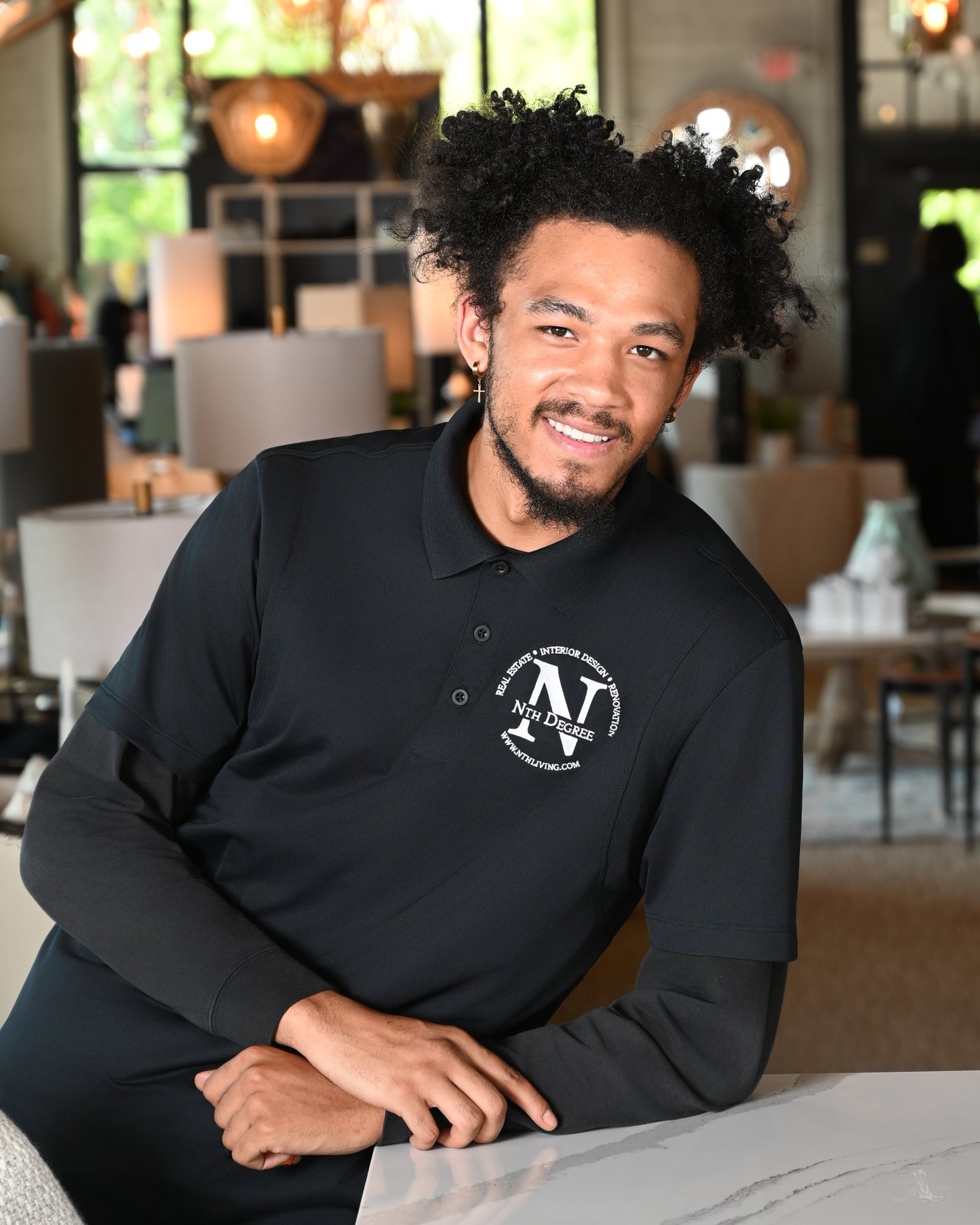 Dejon Drake smiling in a black Nth Degree polo, seated at a marble counter.