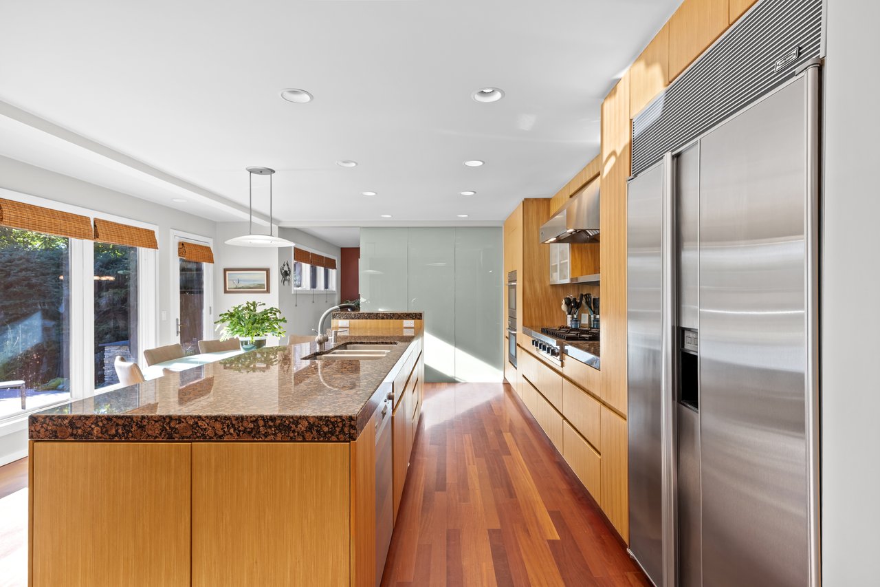 Modern kitchen with a granite island, warm wood cabinetry, and stainless steel appliances.