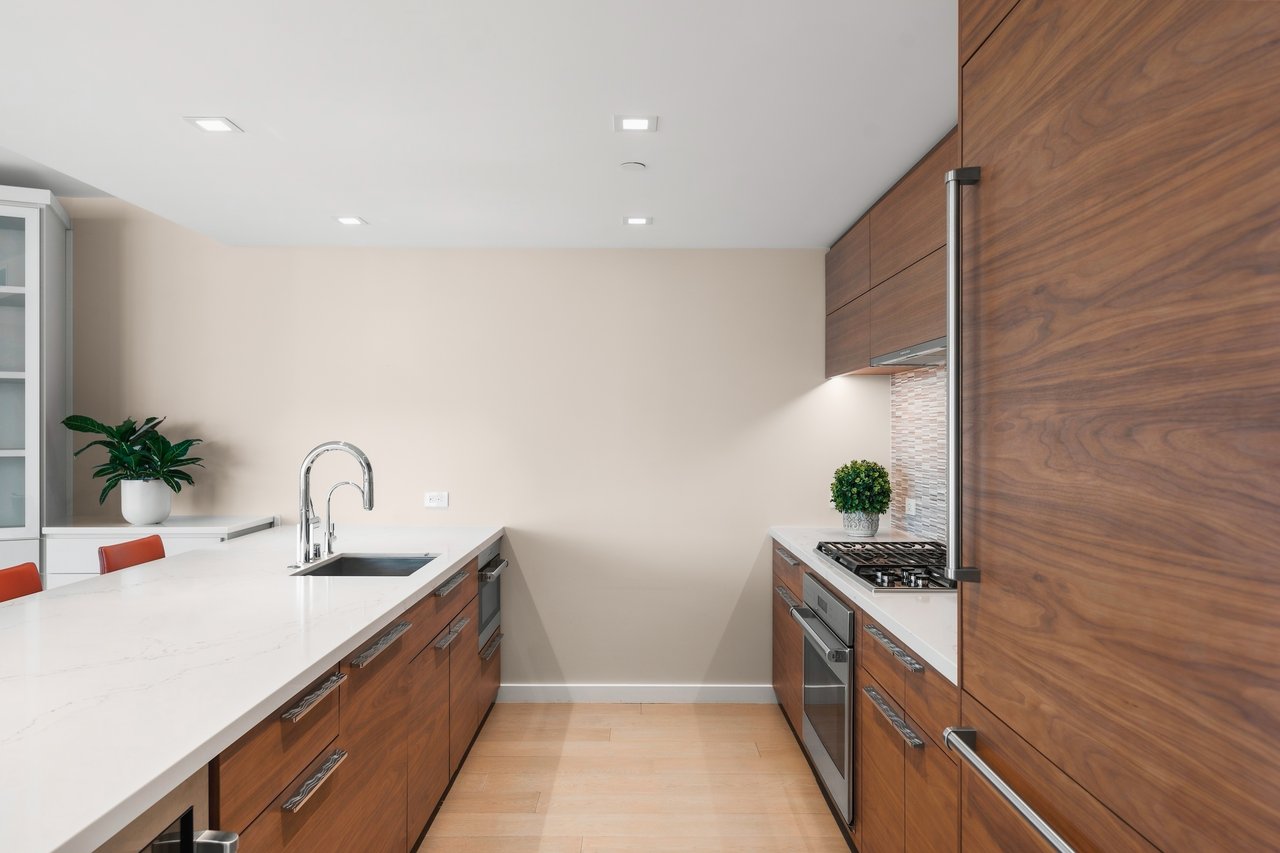 Modern kitchen with walnut cabinets, white stone counters, a broad island, and stainless steel appliances.
