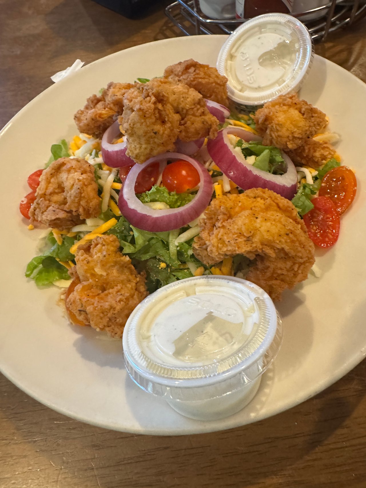 Salad topped with crispy fried chicken, red onion, cherry tomatoes, and two cups of creamy dressing.