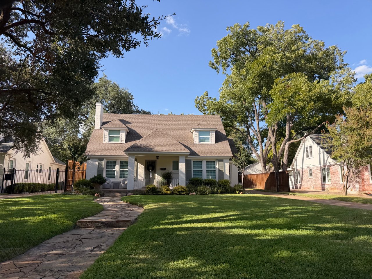 Light-colored house with twin dormers, a covered porch, and a stone walkway across the lawn.