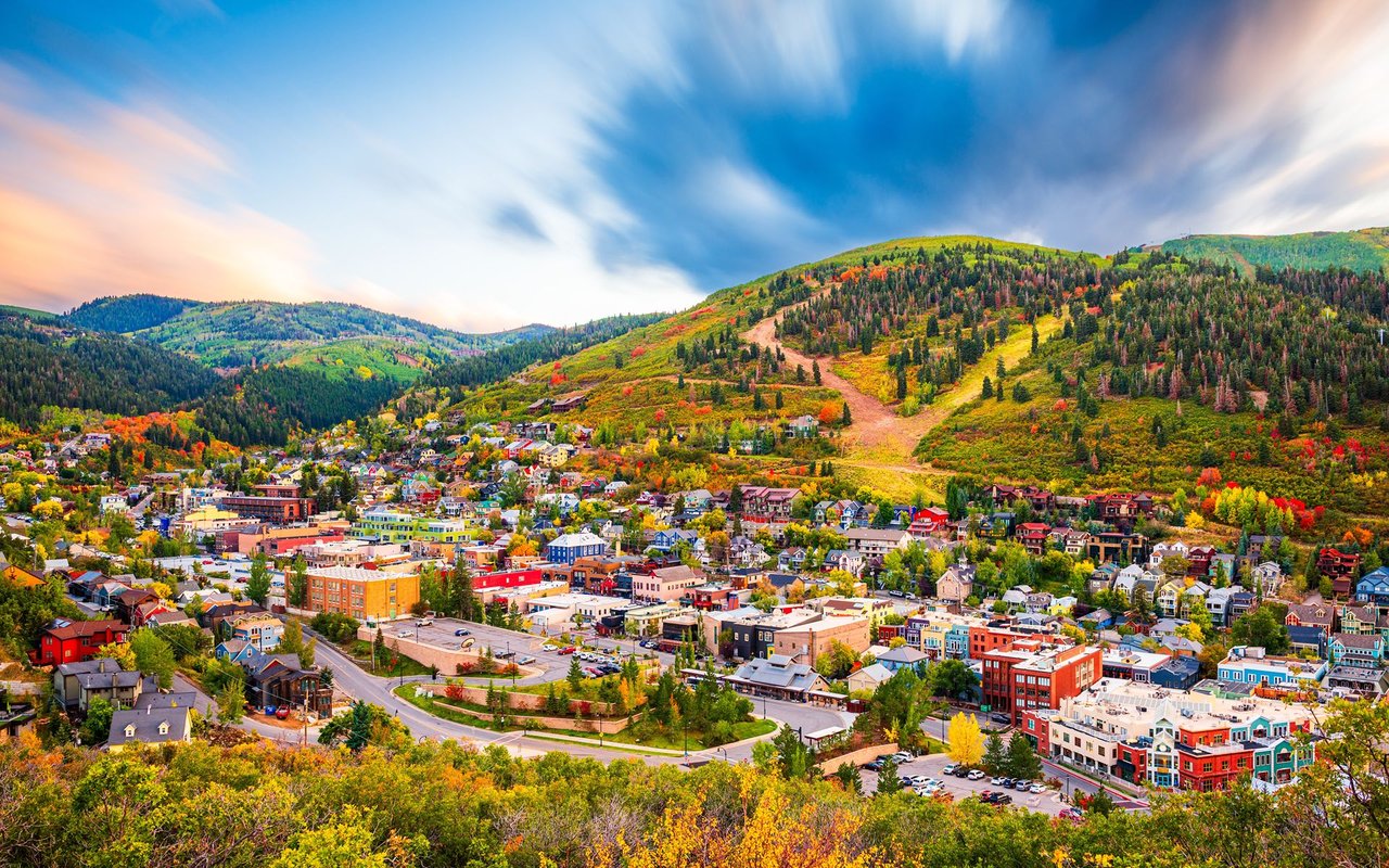 Park City beneath autumn-colored ski slopes, with a colorful downtown and dramatic sunset sky.