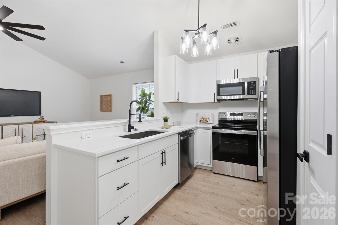 Bright white kitchen with a large island, black fixtures, stainless steel appliances, and an adjoining living area.
