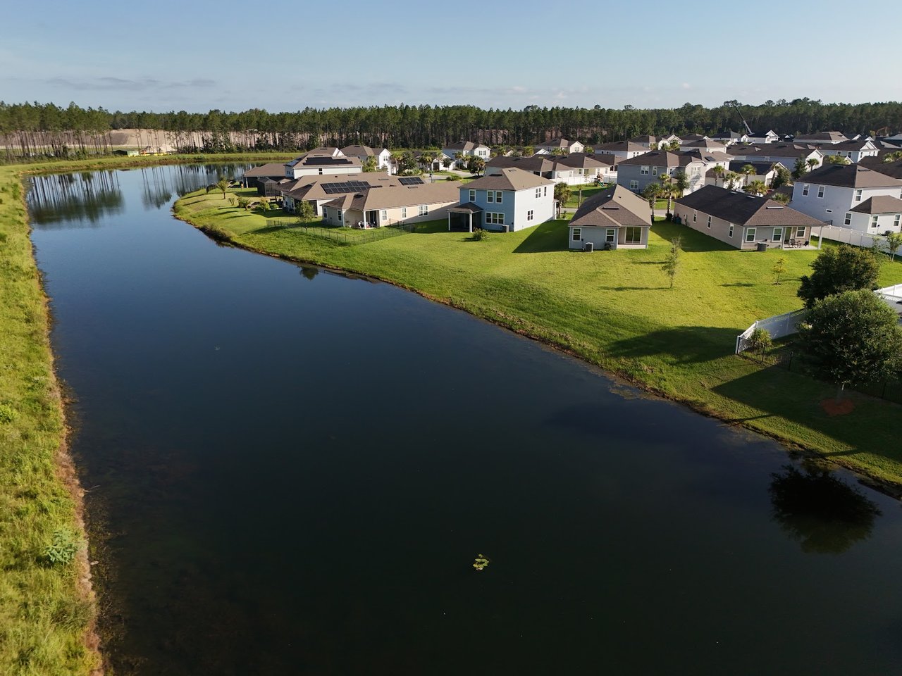 Aerial view of homes beside a pond, with broad lawns and a wooded tree line.