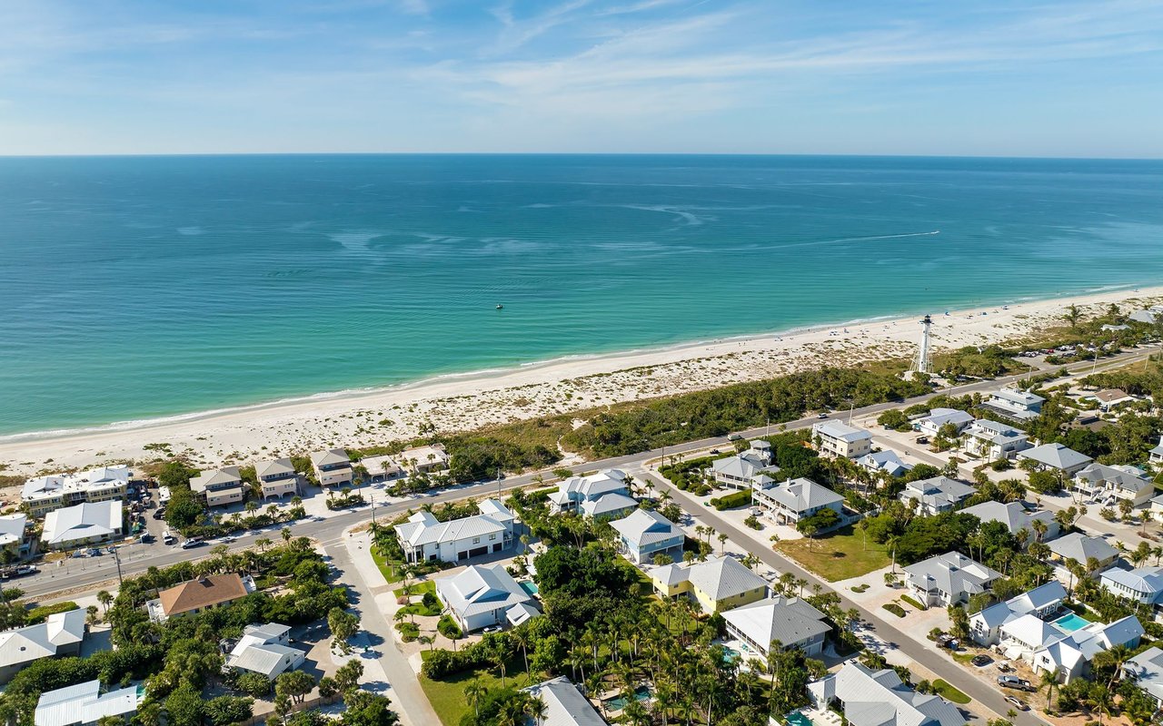 Aerial view of a coastal neighborhood along a sandy beach and turquoise water.