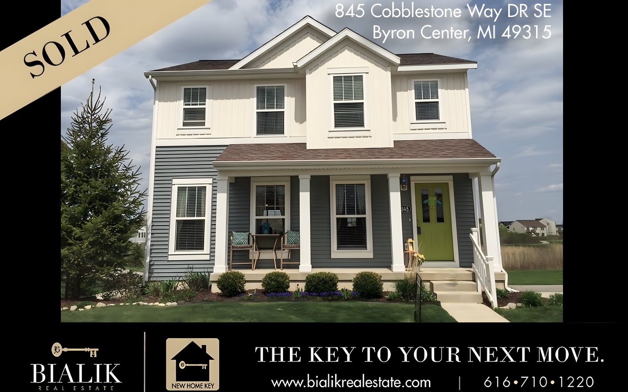 Two-story gray-and-white house with a green front door, porch seating, and a SOLD banner.