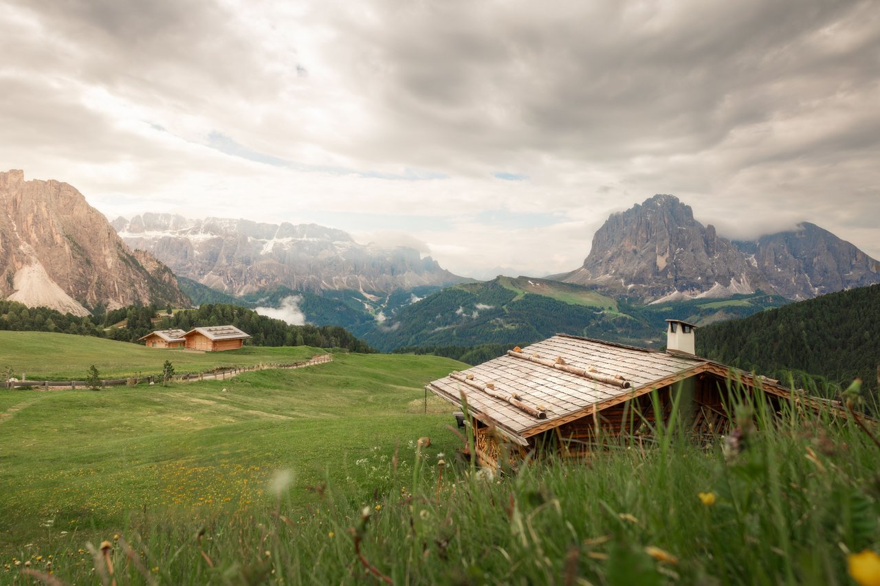 Rustic cabins in a green mountain meadow beneath dramatic rocky peaks.