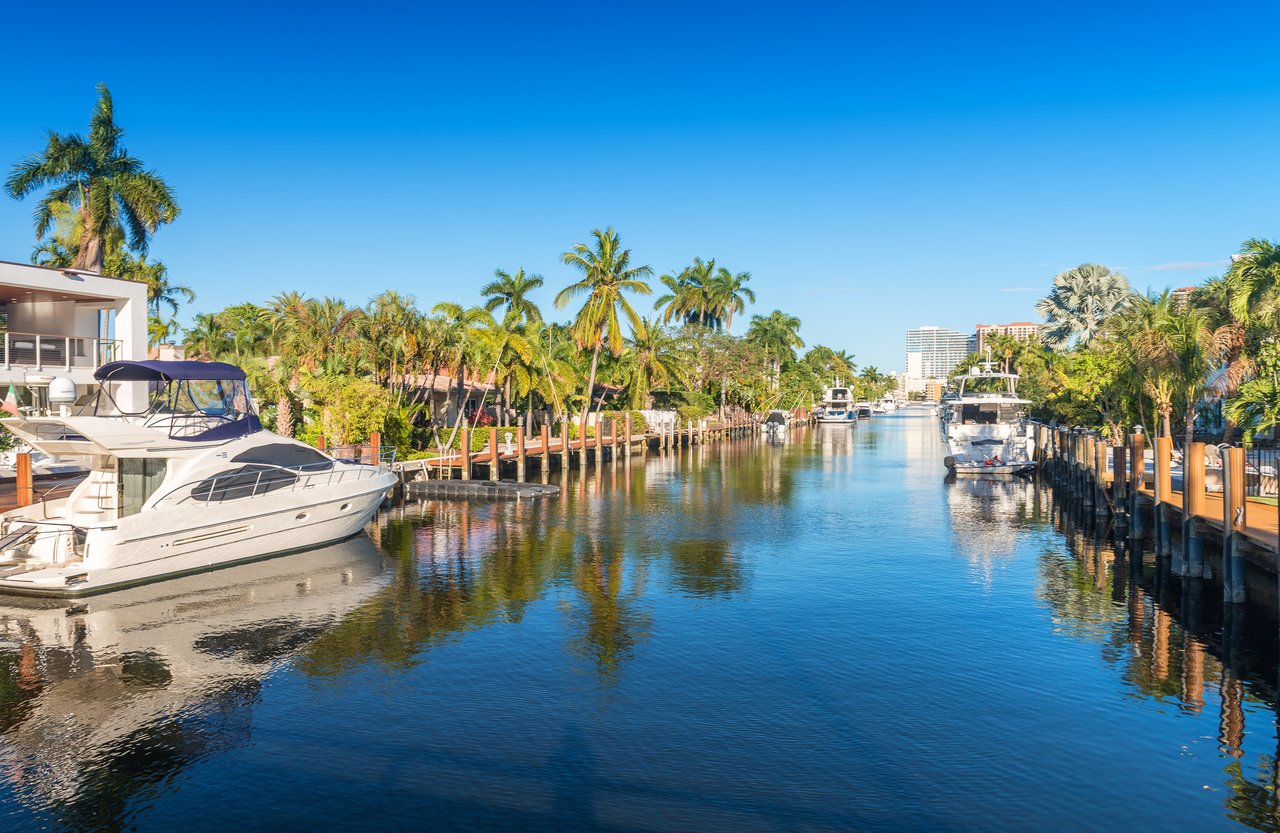 Royal Harbor canal lined with palm trees, waterfront homes, docks, and boats.