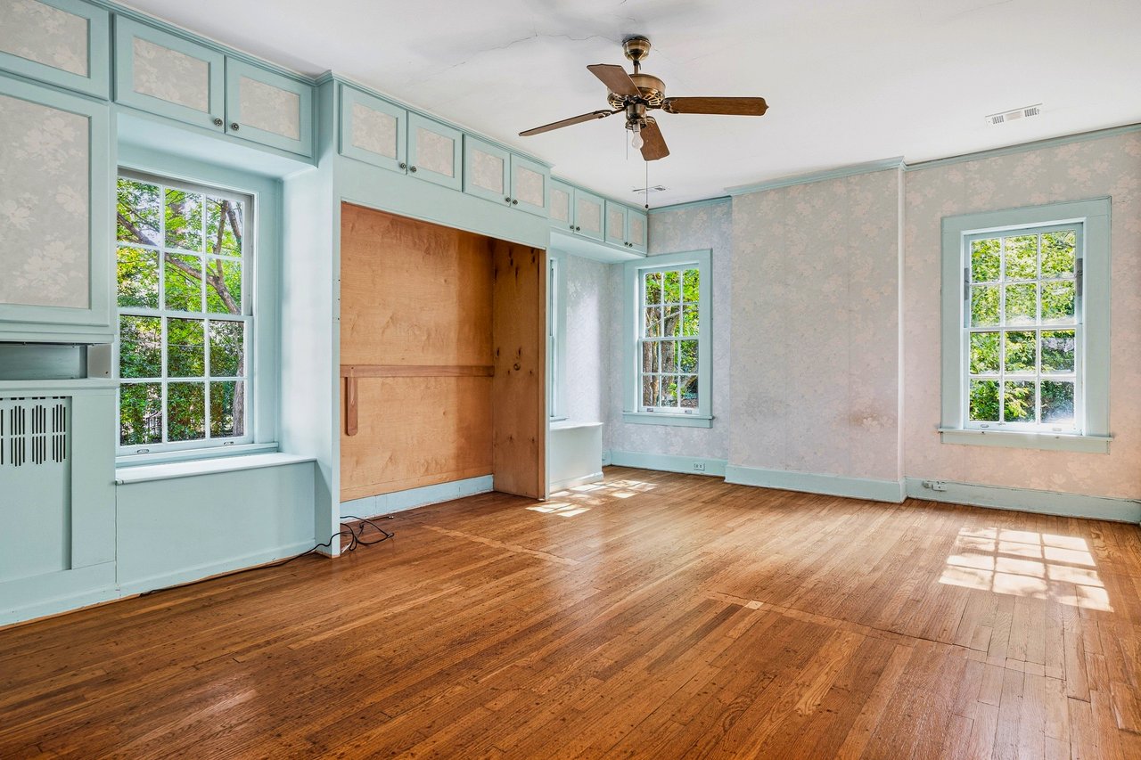 Empty room with hardwood floors, pale aqua built-ins, three windows, and a ceiling fan.