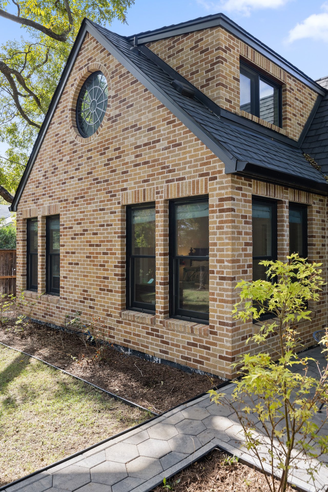 Brick house with a circular gable window, black-framed windows, and a paved garden walkway.