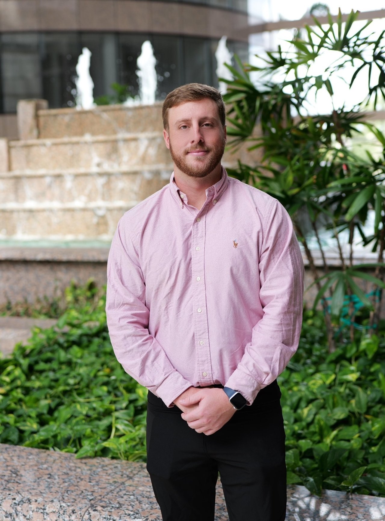 Nicholas Seagroves standing in a courtyard beside a stone fountain and greenery.